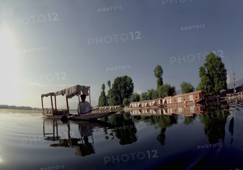 INDIA, Kashmir, Srinagar, Nagin Lake. Man in Shikara or Water Taxi with two modern houseboats moored at the edge of the lake