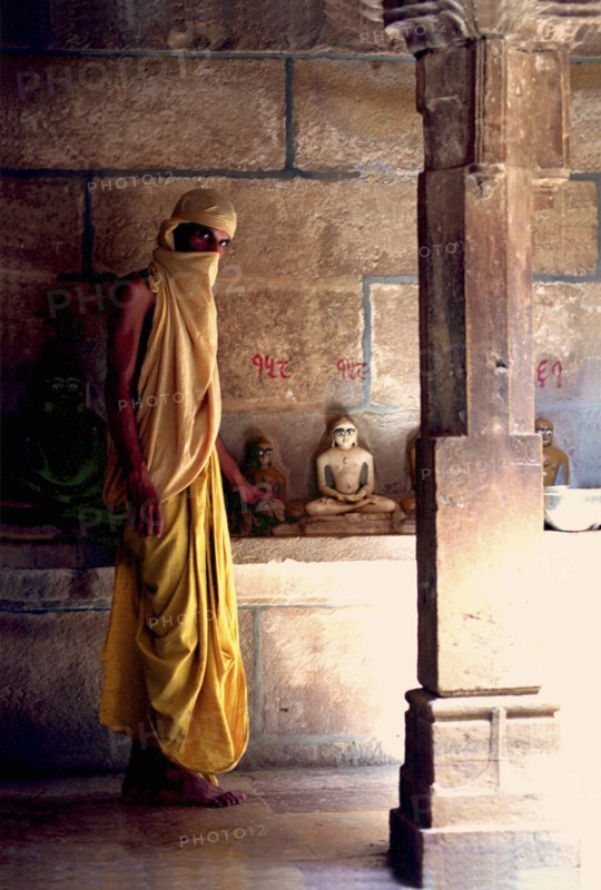 INDIA, Rajasthan, Mt Abu, Fly monk standing near Buddha statues with a scarf covering his head and mouth