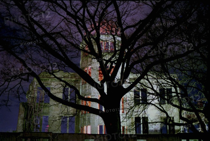 JAPAN, Honshu, Hiroshima, View of the A Bomb Dome illuminated at night seen through silhouetted tree