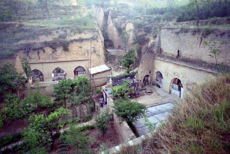 CHINA, Shaanxi, Yulin, View over cave dwellings built into the cliffside with man tending to gardens outside