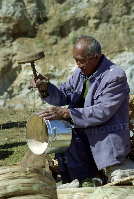 CHINA, Yunnan, Shapin, Man using old style drilling tool on metal and wooden pot