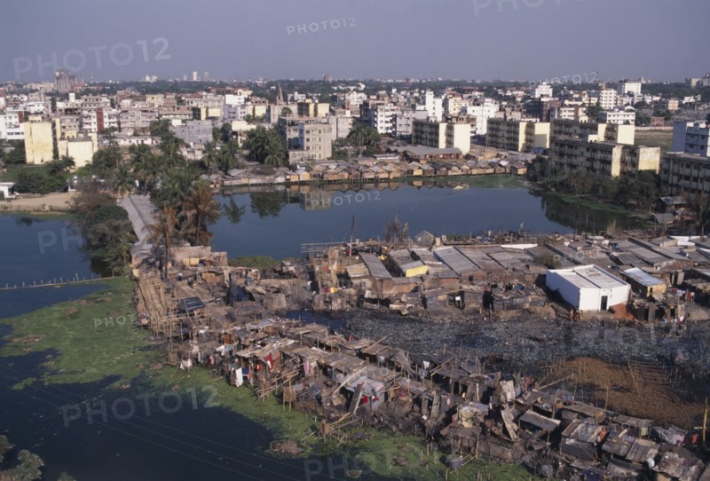 BANGLADESH, Dhaka, Waterside slum dwellings after fire with city buildings beyond.