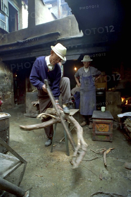CHINA, Tibet, Lhasa, Elderly man cutting firewood for the kitchen in a courtyard