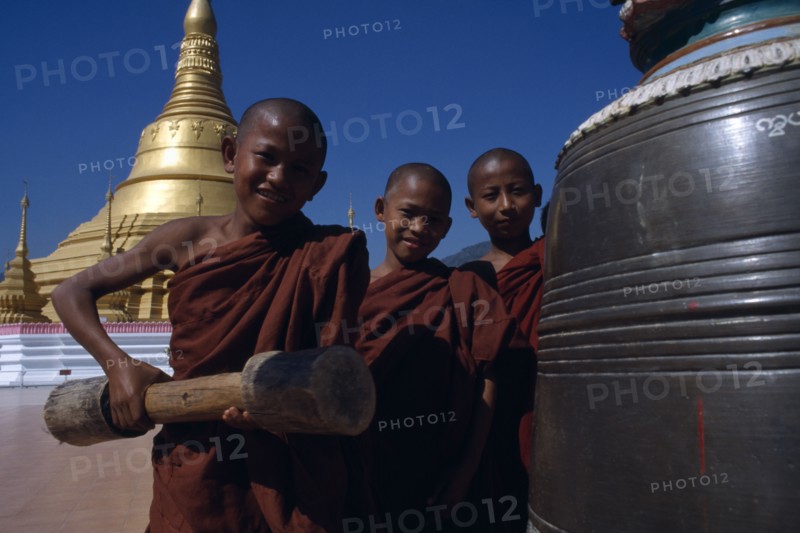 MYANMAR, Thachilek, Young Burmese novice monks at Wat Phra That wao with golden stupa behind.