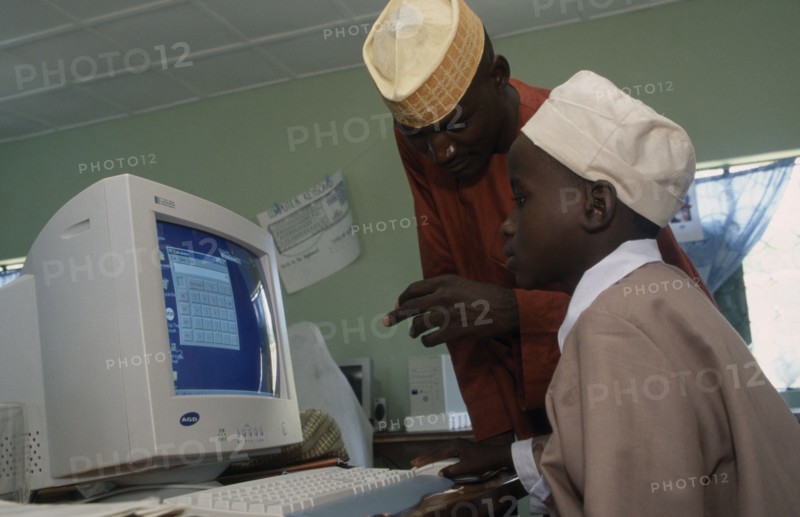 NIGERIA, Education, Teacher leaning over boy sitting at a computer in a classroom