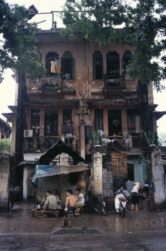 VIETNAM, North, Hanoi, Decayed French colonial style residential buildings with people sheltering from the rain on the pavement