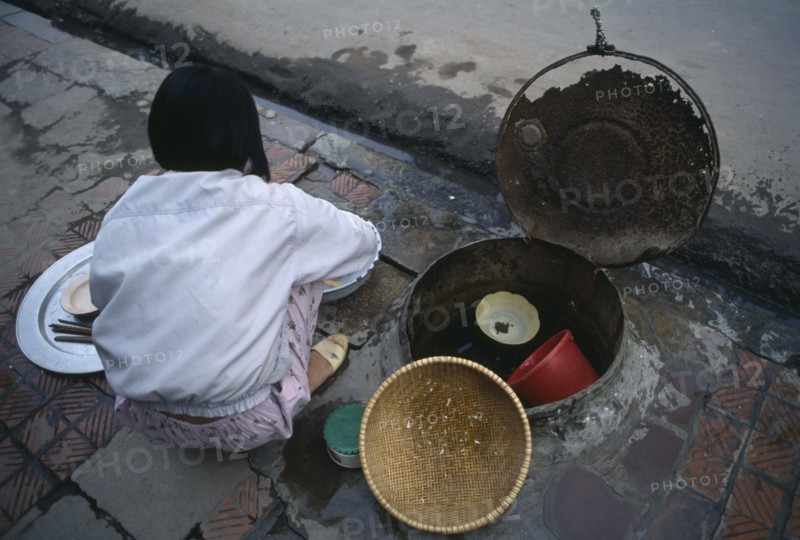 VIETNAM, North, Hanoi, Girl washing pots in a communal water well in the pavement  beside a drain