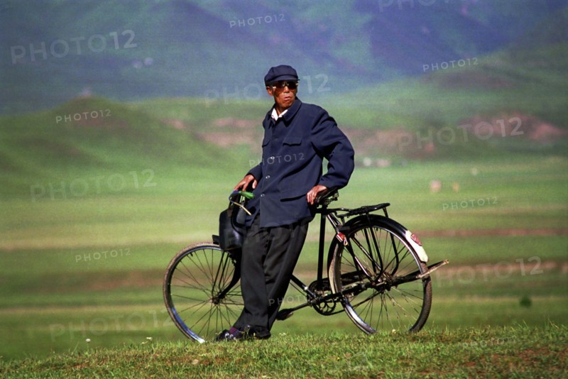 CHINA, Gansu, Xiahe, Weary traveller leaning against bicycle in green landscape