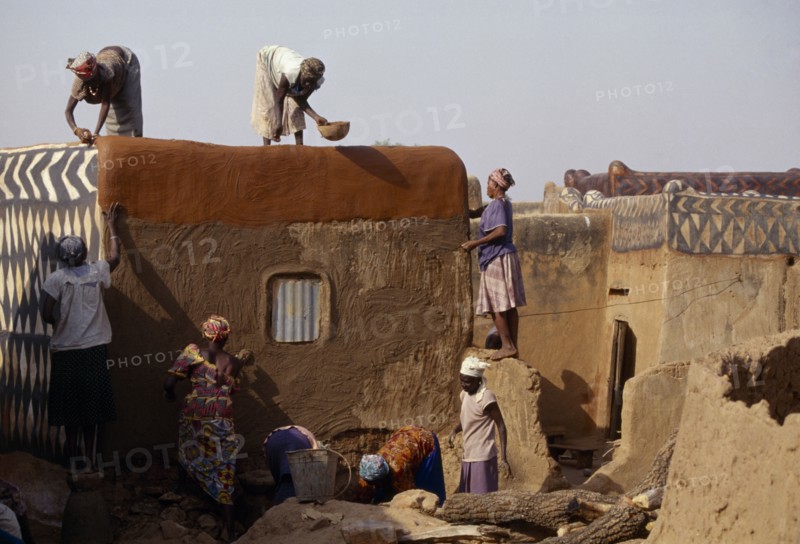 BURKINA FASO, Tiebele, Group of women preparing house front for decorative painting in traditional Gourounsi village.