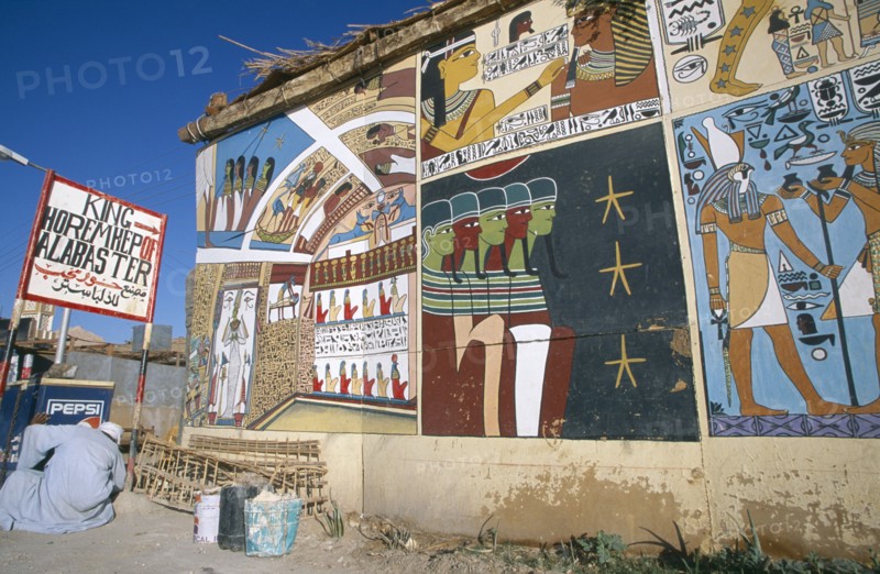 EGYPT, Dra Abul Naga, Painted mural on exterior wall of alabaster shop with man crouched down beside Pepsi sign outside.