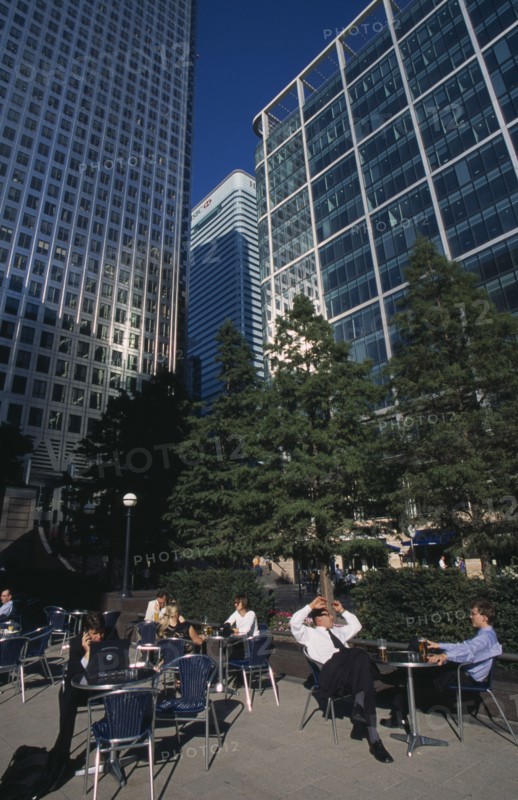 ENGLAND, London, Canary Wharf.  Businessmen and women drinking at outside tables with glass fronted office buildings behind.