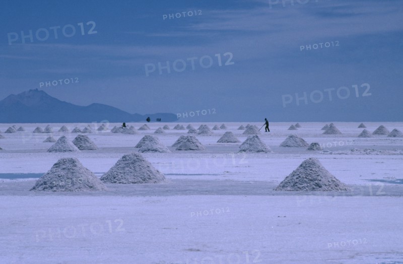 BOLIVIA, Altiplano, Salar de Uyuni, View over the salt plains with figure sweeping up piles of salt for extraction
