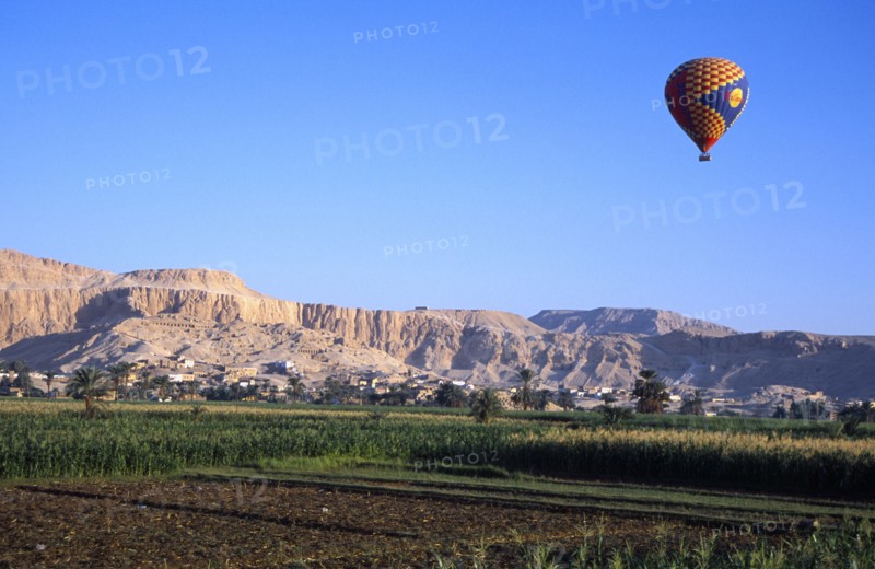 EGYPT, Nile Valley, Thebes, "Valley of the Kings with hot air balloon above agricultural land, village and limestone hills with distant tombs.  "