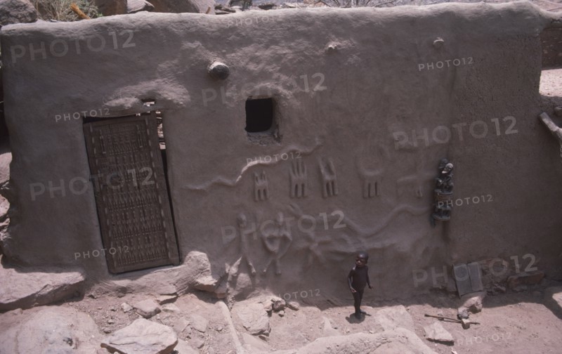 MALI, Dogon village, Detail of exterior wall and door of chiefs house with small child standing outside.