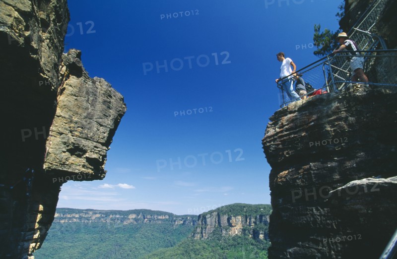 AUSTRALIA, New South Wales, Blue Mountains, View looking up through gap between the Three Sisters cliffs at Katoomba with tourists standing overlooking the edge