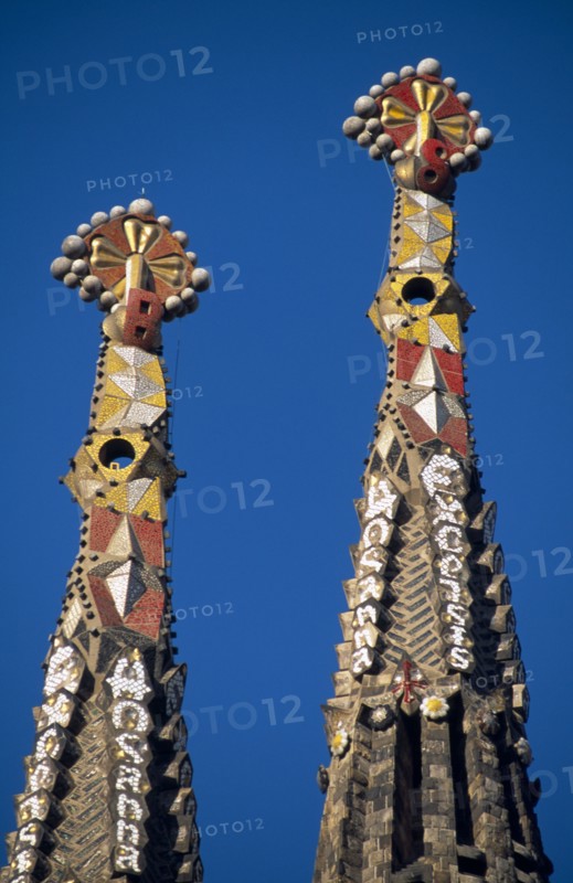 SPAIN, Catalonia, Barcelona, La Sagrada Familia unfinished church designed by Gaudi.  Detail of two spires topped with Venetian mosaic.