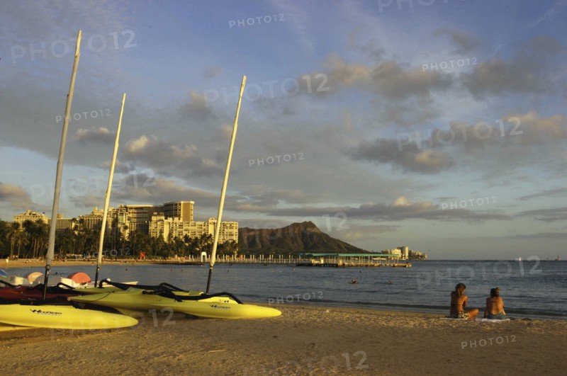 USA, Hawaii, Honolulu, Diamond Head. Sandy beach with two people sitting near boats on the sand in evening light