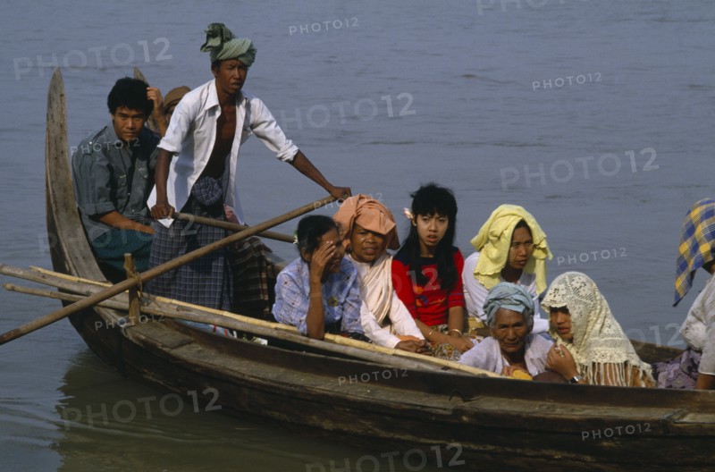 MYANMAR, Irrawaddy River, Man scissor rowing wooden canoe with passengers.