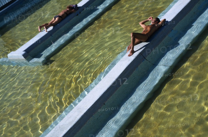 HUNGARY, Budapest, Man and woman lying on raised tiled area above water level in spa.