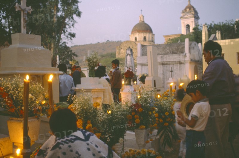 MEXICO, Puebla, Acatlan, People keeping vigil beside graves decorated with candles and flowers during Night of the Dead