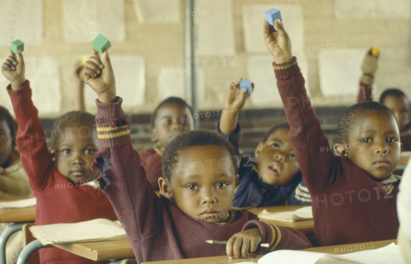 SOUTH AFRICA, Gauteng, Soweto, Classroom scene.  Young pupils raising hands.