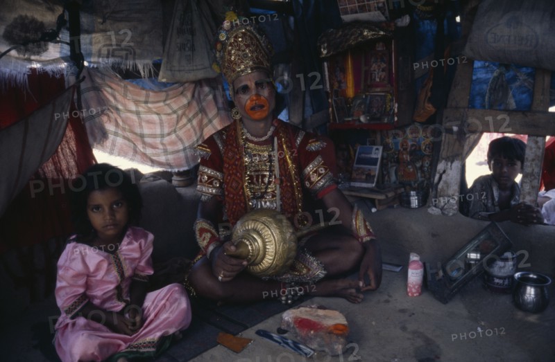 INDIA, Gujarat, Bhavnagar, Man in his shanty house dressed up as the Hindu deity Hanuman.  Child looking in through open window and little girl sitting beside him.