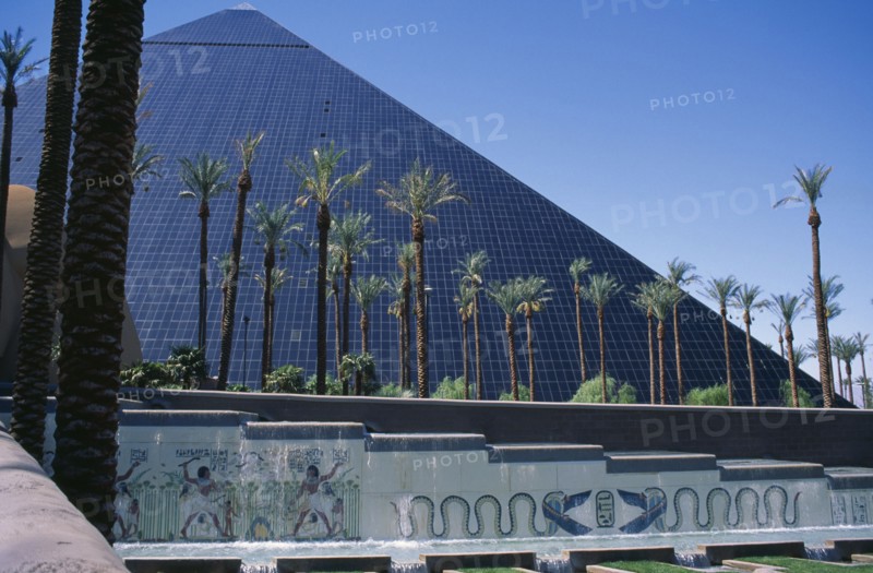 USA, Nevada, Las Vegas, The Luxor Hotel exterior with replica pyramid and hieroglyphics.  Water feature and line of palm trees in the foreground.