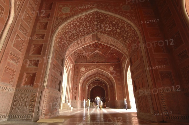INDIA, Uttar Pradesh, Agra, "Taj Mahal, with an 9nterior view of the elaborate red sandstone hallway and arches of the western mosque with people walking through"