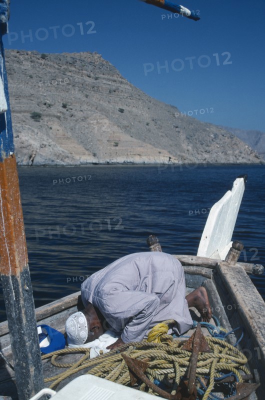 OMAN, Musandum, Fisherman praying on deck of boat.