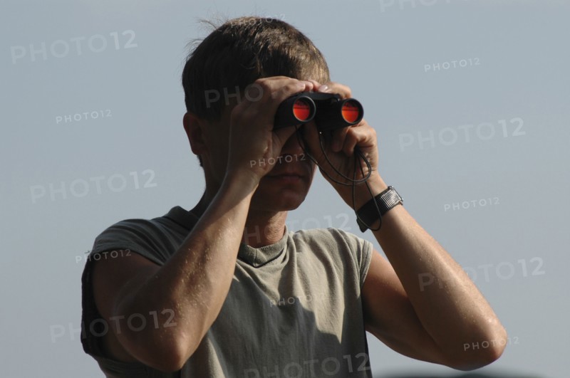 ROMANIA, Tulcea, Danube Delta Biosphere Reserve, Male tourist with binoculars with scenery reflected in orange in his binoculars