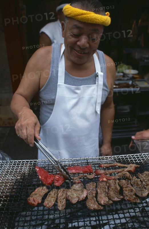 JAPAN, Honshu, Tokyo, Tsukiji Fish Market. Man cooking red meat on an open grill