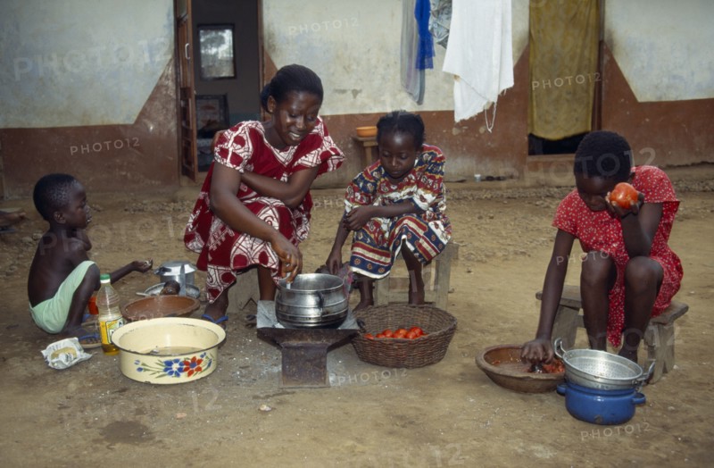 GHANA, Cooking, Woman with children cooking Abenkwan or palm nut soup a thick broth made from the pulp of boiled palm fruit with added fish or meat and spices.