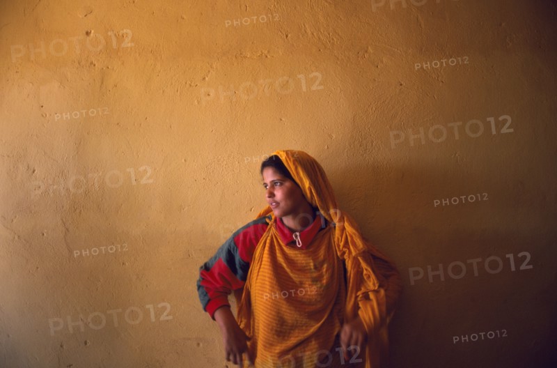 WESTERN SAHARA, Polisario Front, Saharawi girl standing in front of wall painted deep ochre colour.
