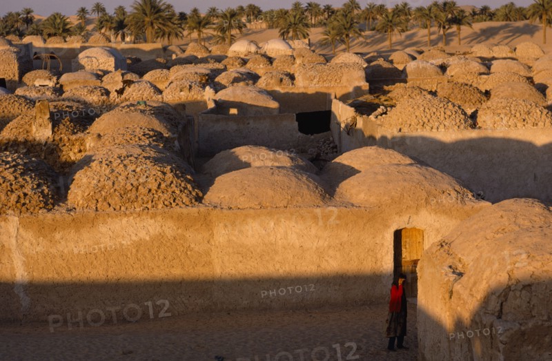 20032915 ALGERIA  Architecture Typical mud architecture with woman wearing red standing in the foreground.