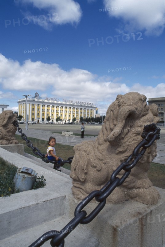 MONGOLIA, Ulan Bator, Sukhbaatar square with small girl sitting on chainlink fence around steps in foreground.