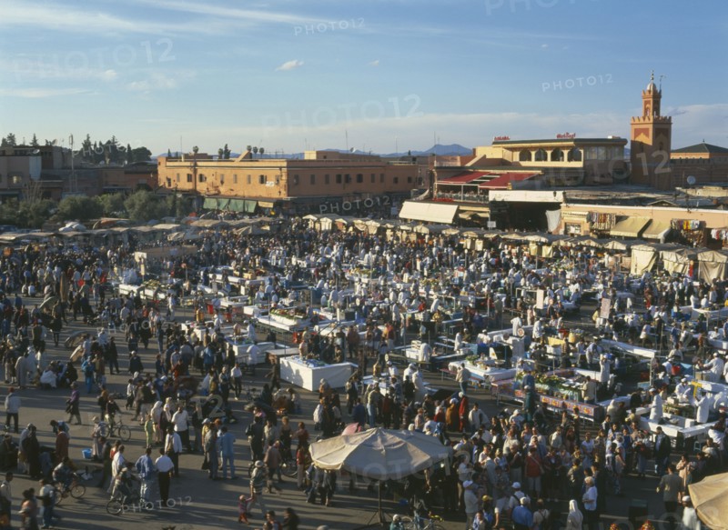 MOROCCO, Marrakech, Djemaa El Fina Square. View over busy market square with crowds of people at stalls and buildings behind.