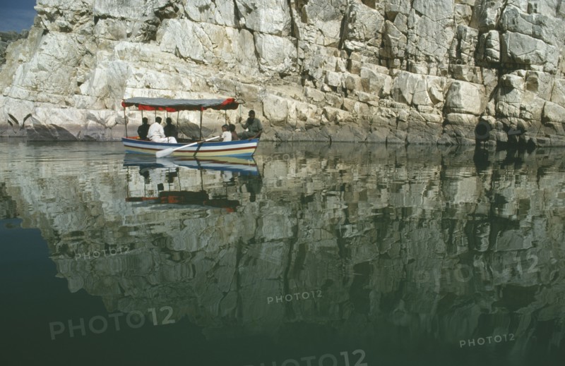 INDIA, Madhya Pradesh, Marble Rocks, Painted tourist boat on the Narmada River passing sheer cliffs reflected in water.