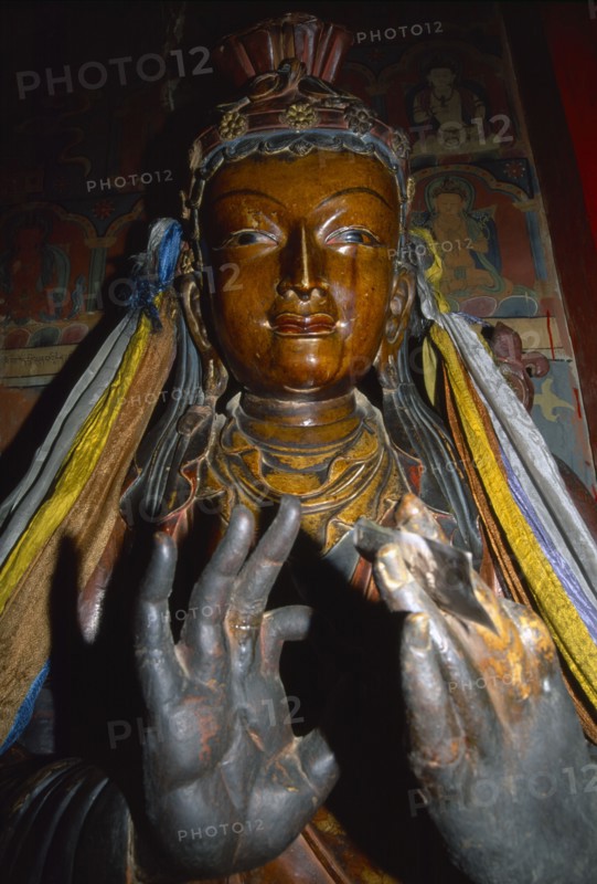 TIBET, Gyantse, Interior of the Assembly Hall with a figure of a Buddha with hands in the foreground and paintings on the wall behind.