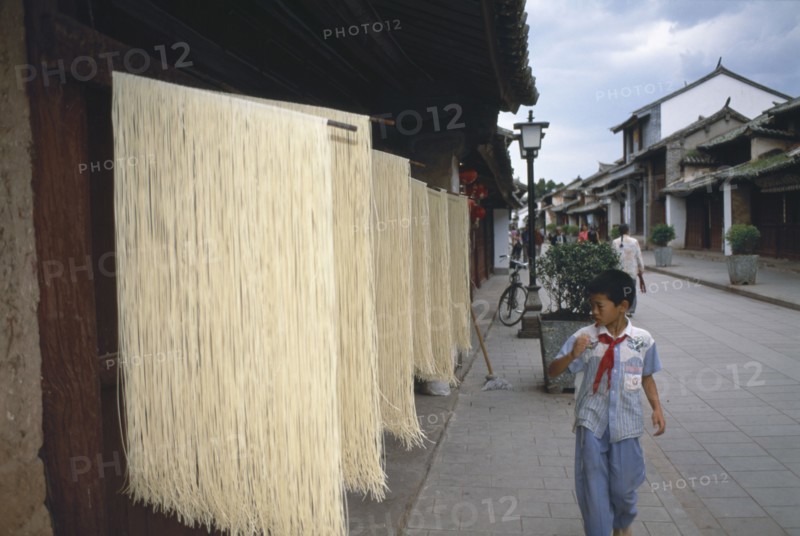 CHINA, Yunnan, Dali., Weishan. Racks of noodles hanging out to dry in street with a boy walking past on pavement.