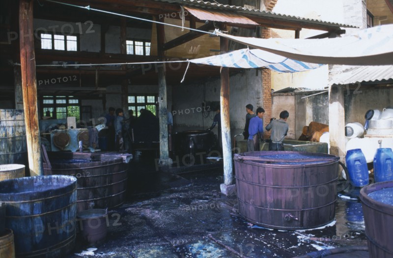 CHINA, Yunnan , Dali, Weishan. Batik factory with men working around  vats of dye under ornings.