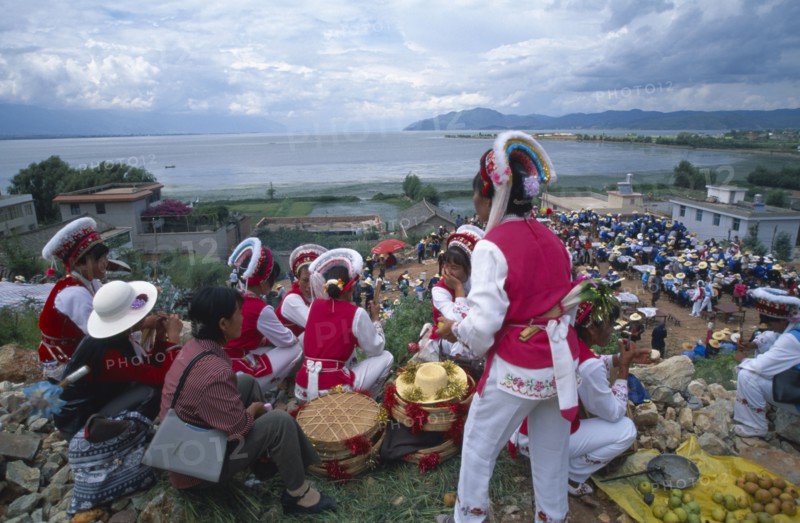 CHINA, Yunnan, Dali, Group of Bai ethnic minority girls in traditonal costume above a market with the sea in the distance.