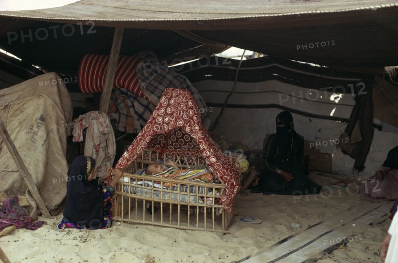 MIDDLE EAST, People, Bedouin desert encampment.  Woman and children inside tent with baby in traditional cradle