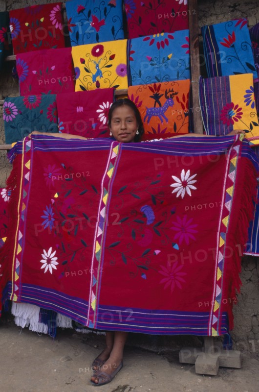 MEXICO, Chiapas, Zinacantan, Young girl holding up brightly coloured embroidered local cloth for sale.