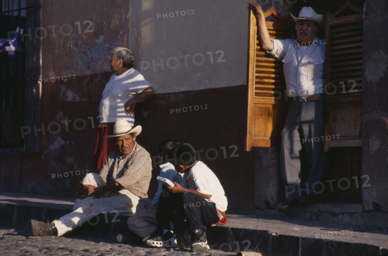 MEXICO, Guanajuato, San Miguel de Allende, Street scene with man and young boys in conversation sitting on pavement and man and woman standing behind.