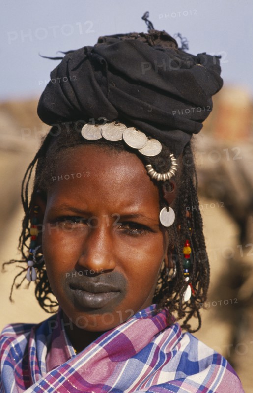 MALI, Tribal People, Head and shoulders portrait of Fulani woman with tattooed lips and wearing French coins in her hair.