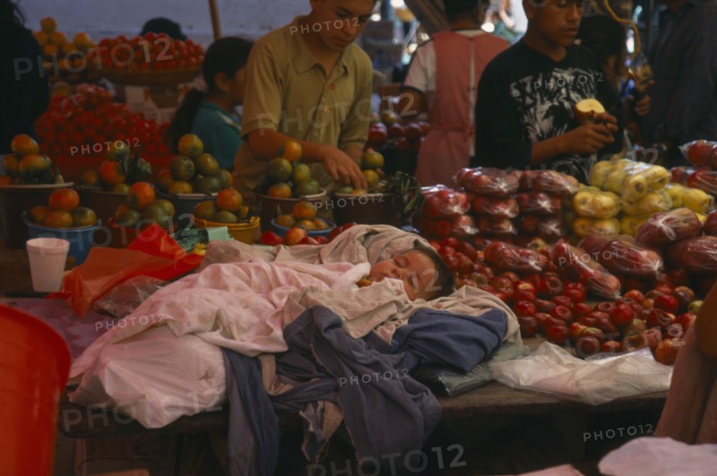 MEXICO, Oaxaca, Sleeping child on market stall selling fruit.