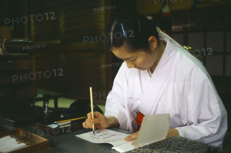 JAPAN, Honshu, Tokyo, Meiji Jingu Shrine.  Japanese woman writing at desk using brush and ink.