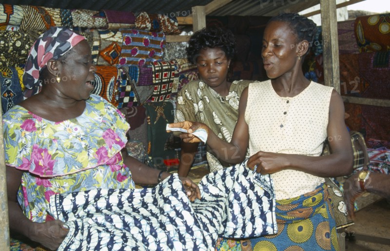 GHANA, West, Markets, Woman purchasing length of batik dyed cloth with fish design from market vendor.