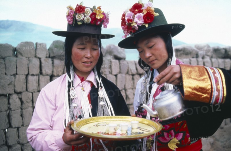 CHINA, Qinghai Province, Huzhu County, Women of Tu nationality and Lamaist Buddhist Yellow Hat sect preparing traditional welcome of three small glasses of alcoholic drink.
