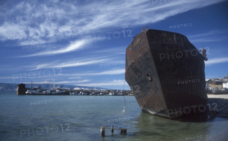 RUSSIA, Siberia, Lake Baikal, Rusting hull of ship in shallow water at lake shore.